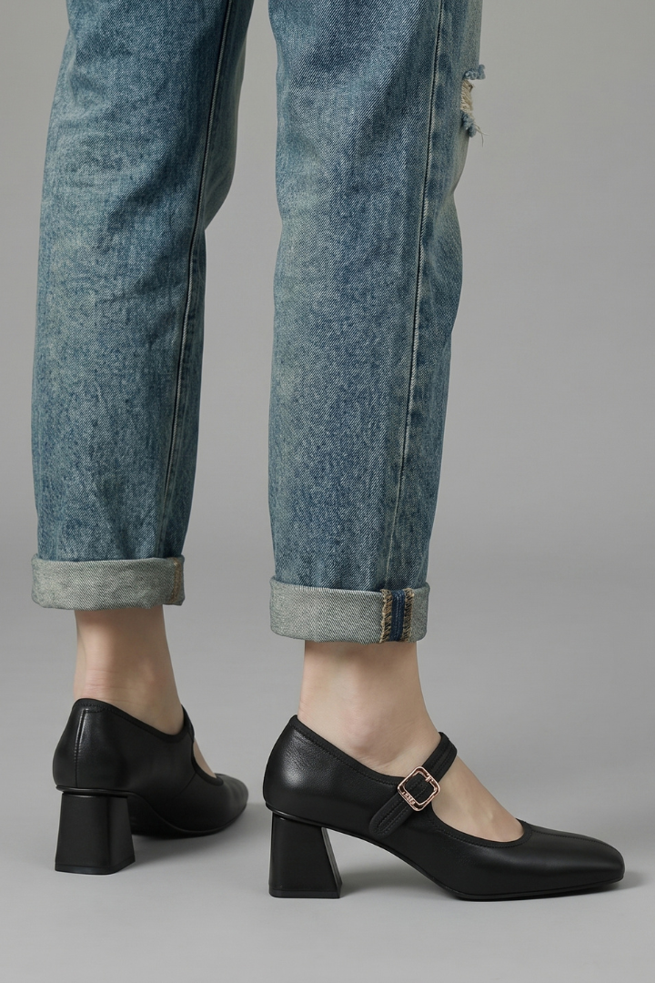 Black shoes worn with rolled-up blue jeans on a gray background