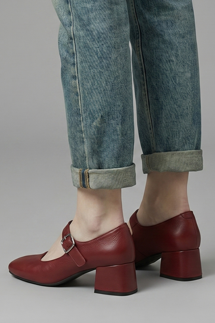 Red shoes with a block heel worn with rolled-up jeans on a neutral background
