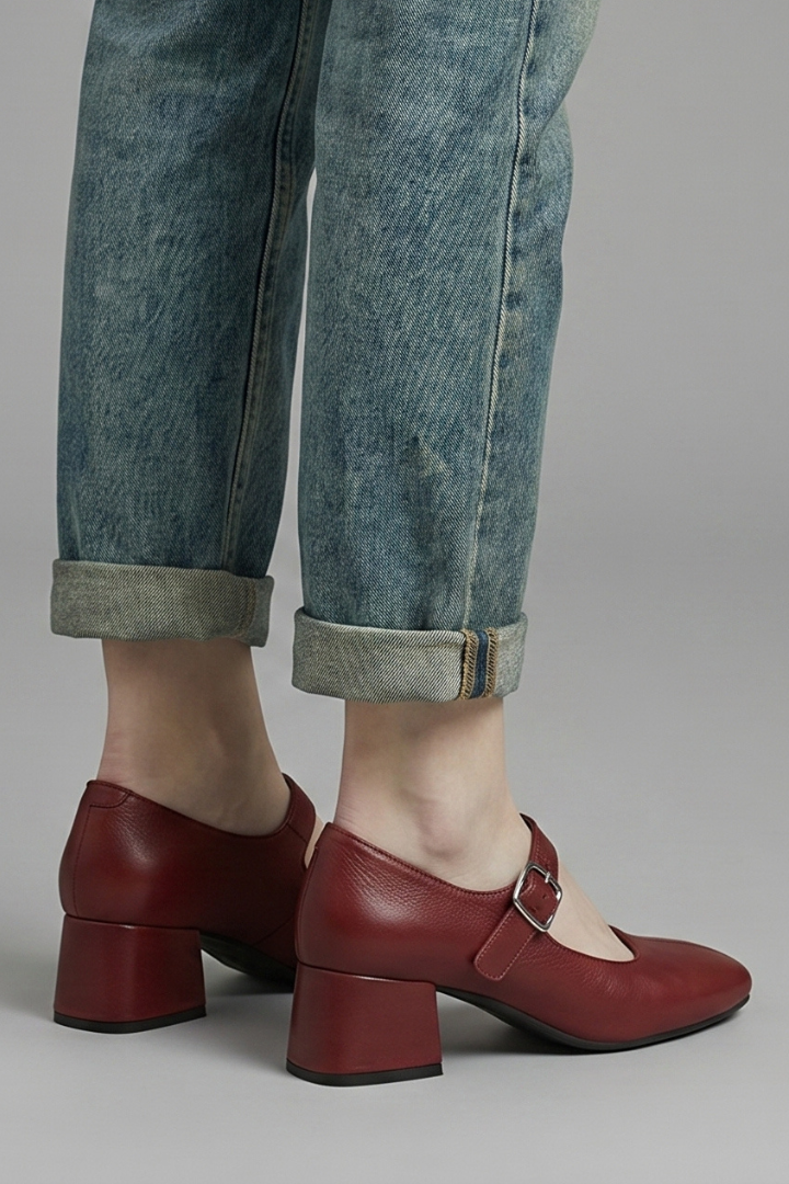 Red shoes worn with rolled-up jeans on a neutral background