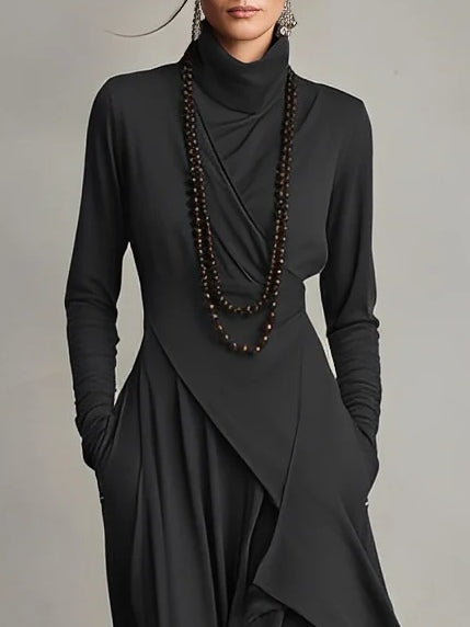 Woman wearing a black dress with a draped design and a long necklace against a gray background