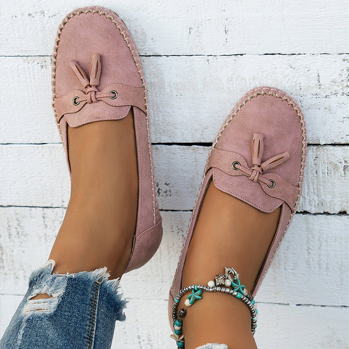 Pink loafers worn with ripped jeans on a white wooden floor.