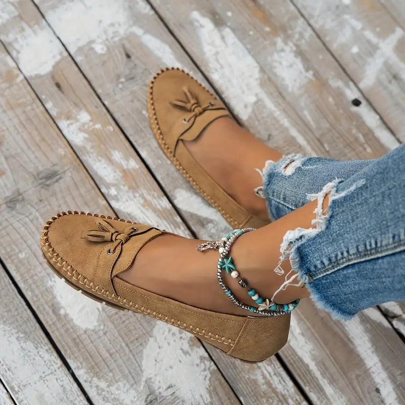 Tan loafers worn with ripped jeans on a wooden floor
