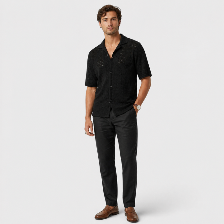 Man wearing a black patterned shirt and black pants on a white background