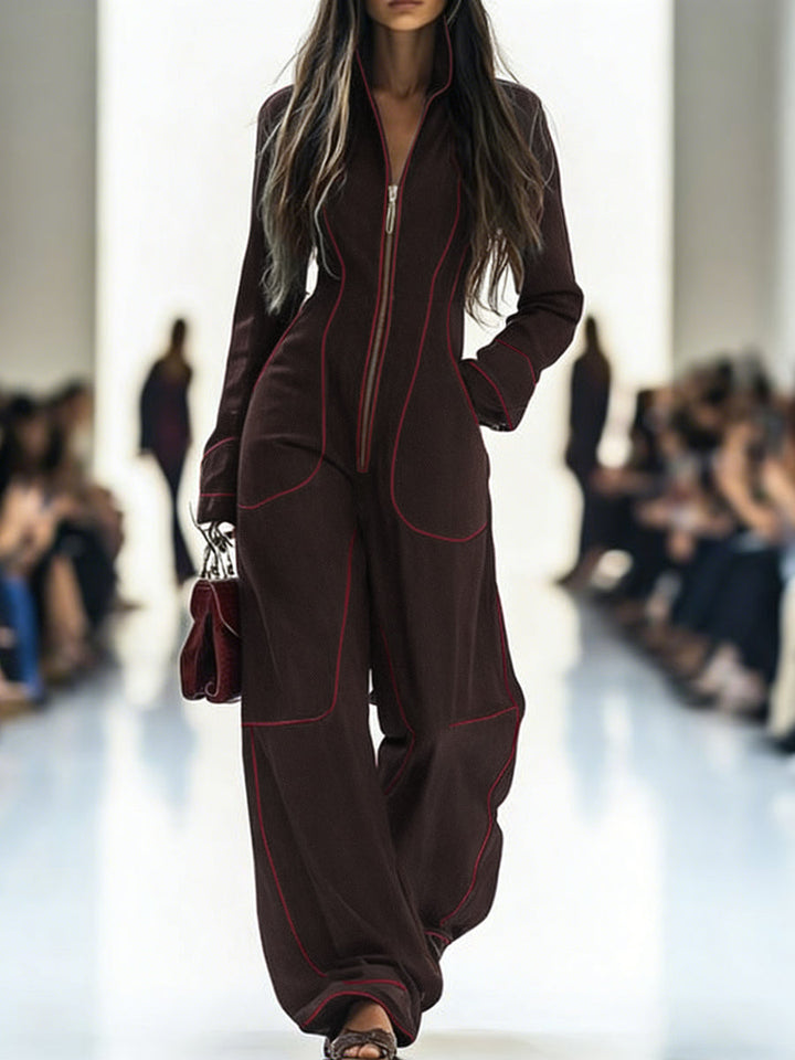 Model wearing a brown jumpsuit with red piping on a runway.