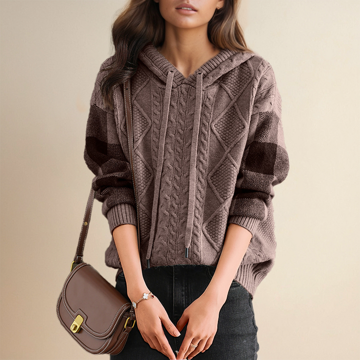 Person wearing a cable knit hoodie with a brown handbag on a beige background