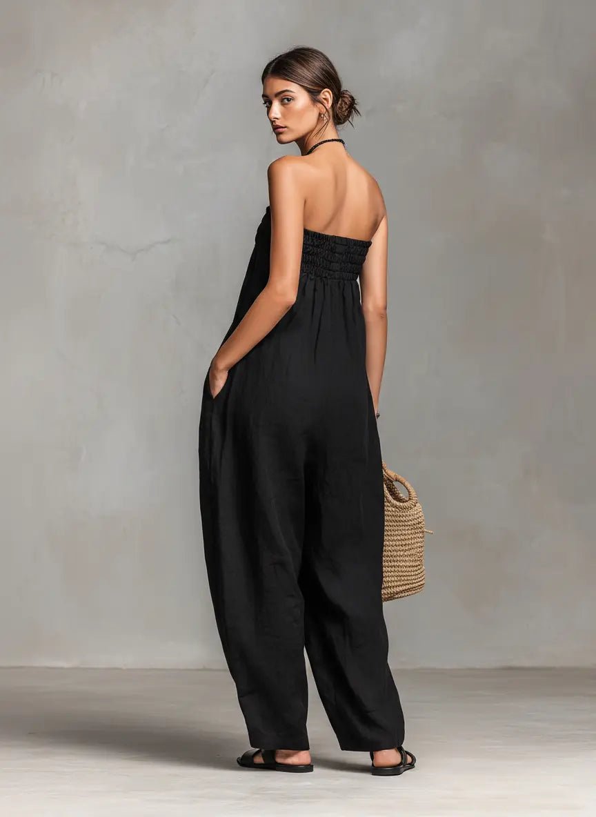 Woman wearing a black jumpsuit holding a woven bag against a gray background
