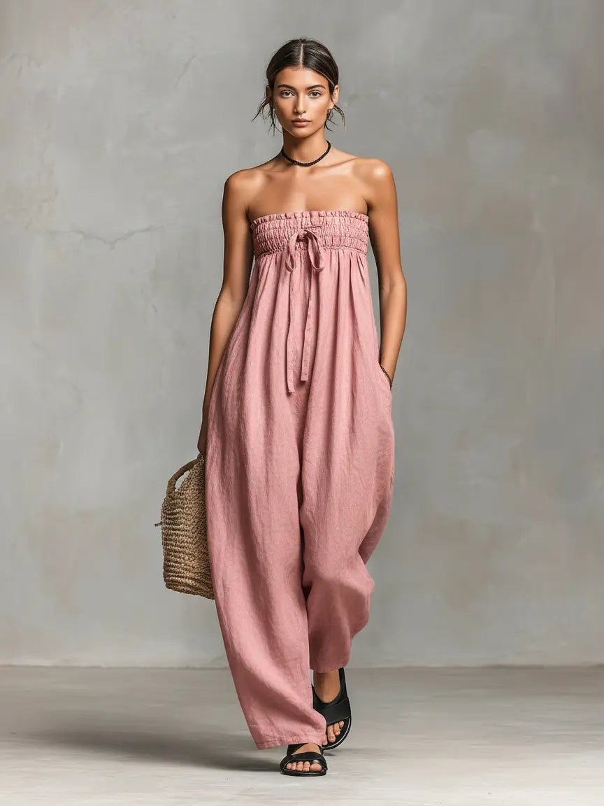 Woman wearing a pink strapless jumpsuit holding a woven bag against a neutral background