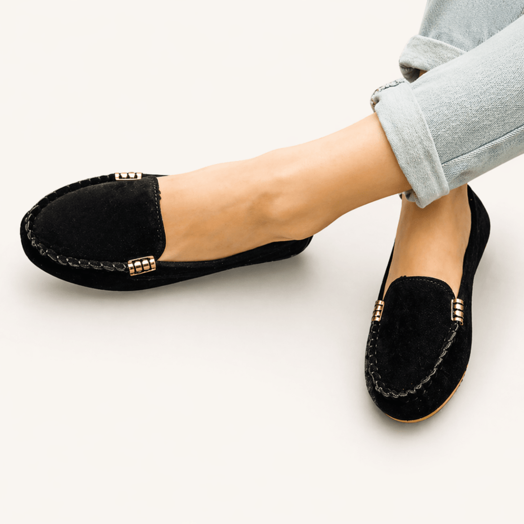 Black loafers with gold accents worn by a person on a light background