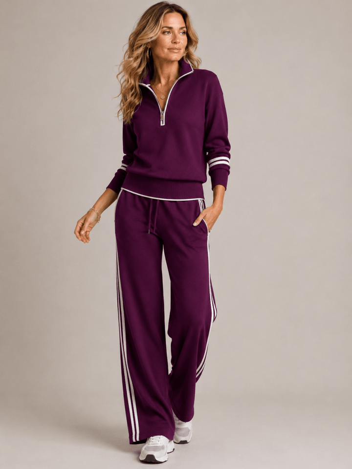 Woman wearing a purple tracksuit with white stripes on a plain background