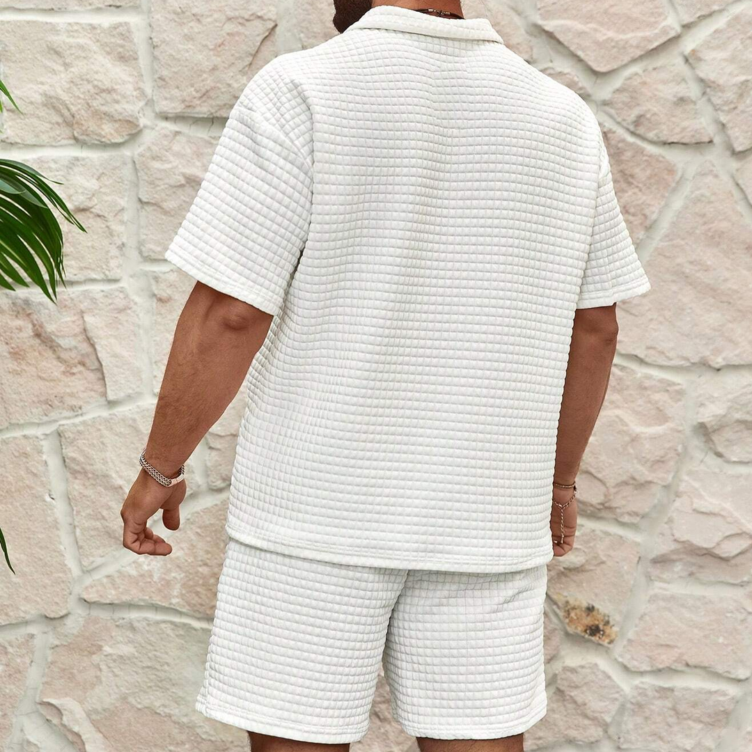 Person wearing a textured white outfit standing against a stone wall.