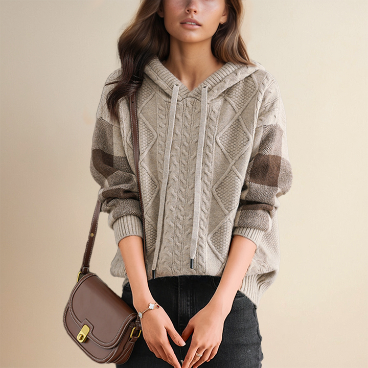 Woman wearing a cable knit hoodie with a brown handbag on a beige background