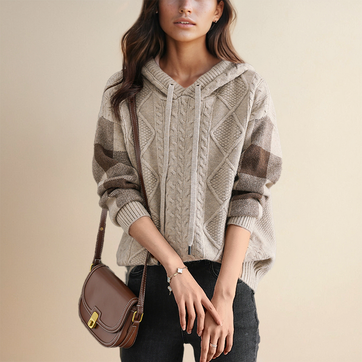 Woman wearing a cable knit sweater holding a brown handbag against a beige background