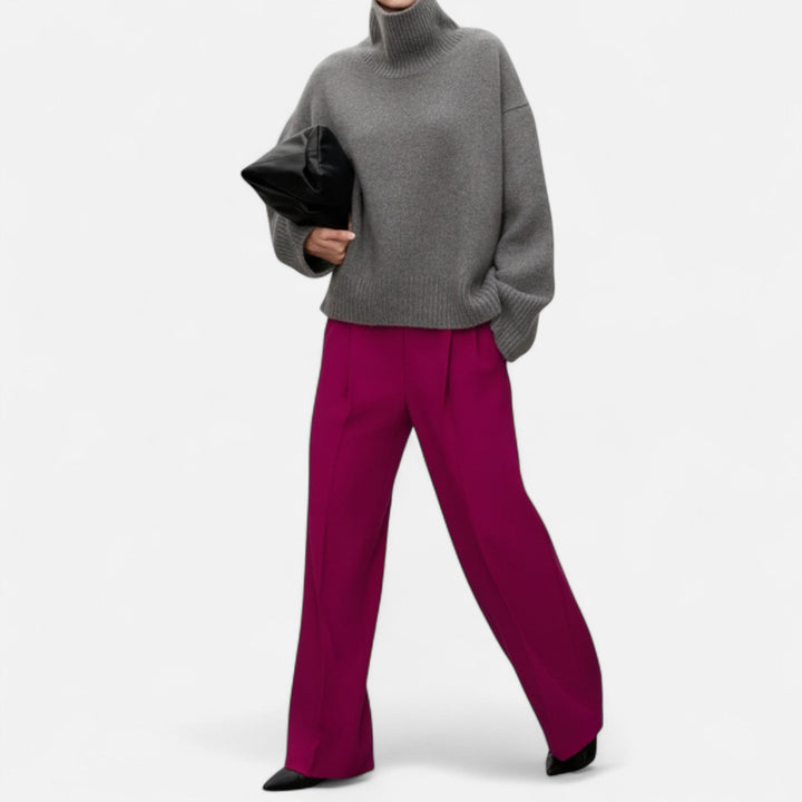 Person wearing a gray sweater and magenta pants holding a black clutch on a white background