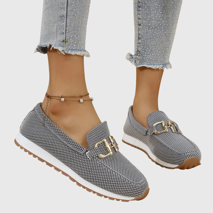 Gray loafers with gold buckles worn by a person on a light gray background