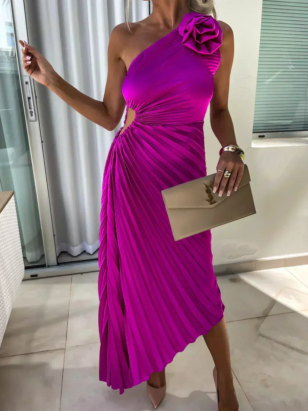 Woman wearing a vibrant purple one-shoulder dress with a floral detail, holding a beige clutch.