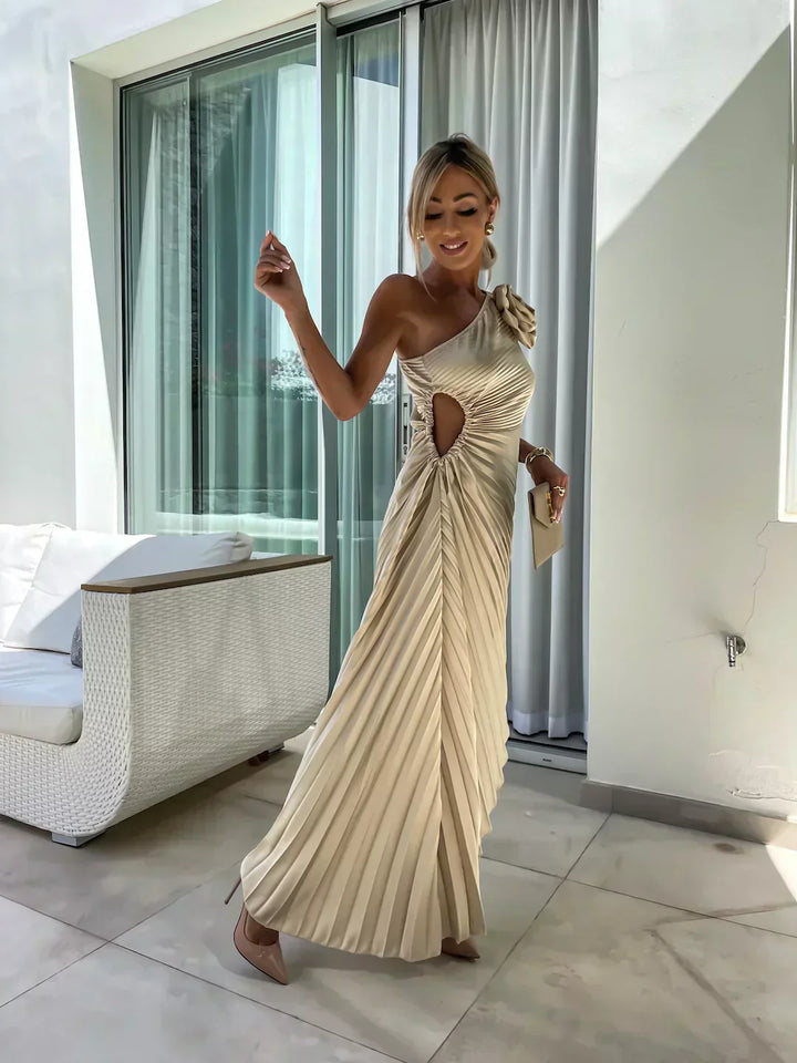 Woman in a beige pleated dress standing in a modern indoor setting.