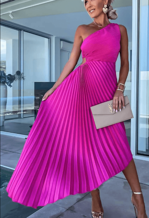 Woman wearing a bright pink pleated dress holding a beige clutch in an indoor setting.