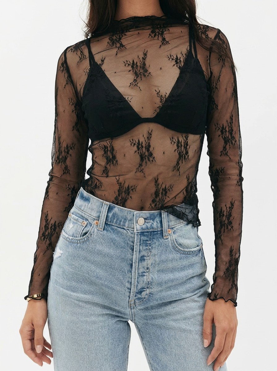 Person wearing a sheer black lace long-sleeve top over a black bralette with high-waisted blue jeans.