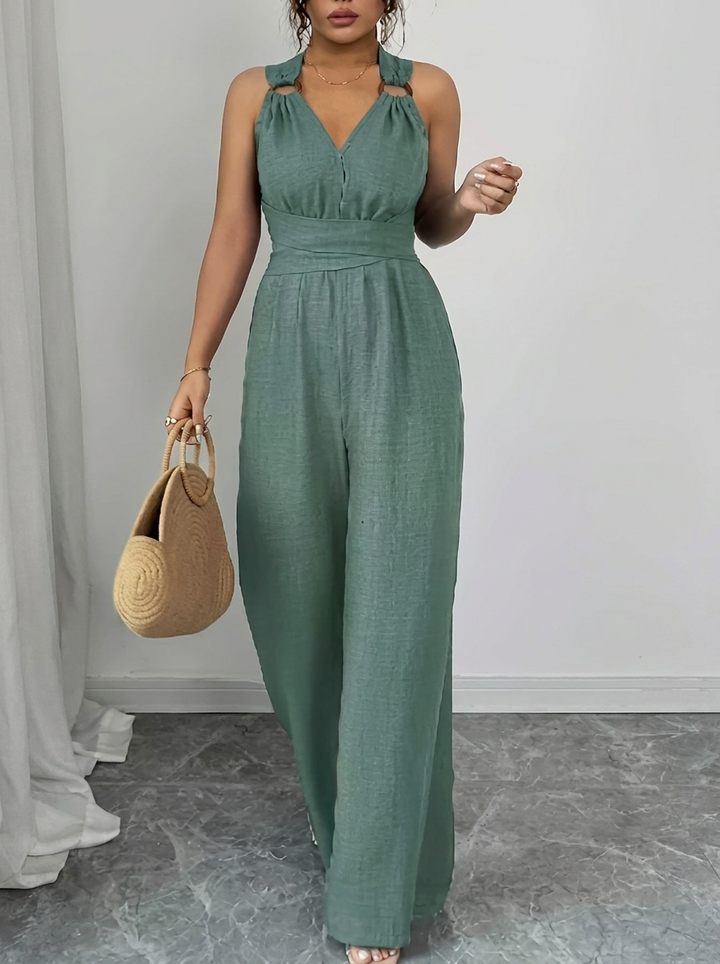 Woman wearing a green jumpsuit holding a beige handbag against a neutral background