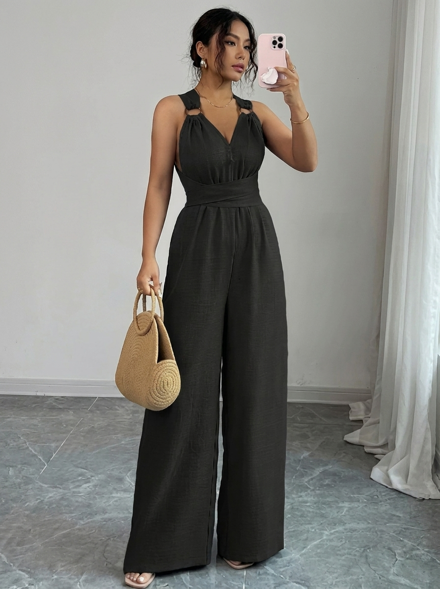 Woman in a black jumpsuit taking a mirror selfie in a room with a gray floor and white walls.