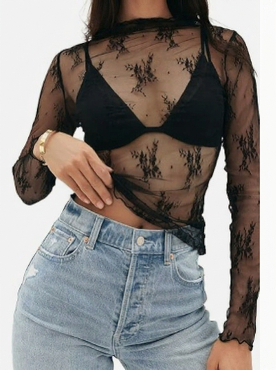 Person wearing a sheer black top with floral patterns and high-waisted blue jeans.