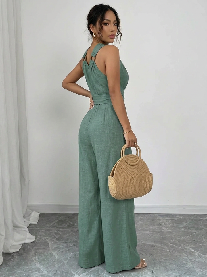 Woman wearing a green jumpsuit holding a woven handbag against a white background