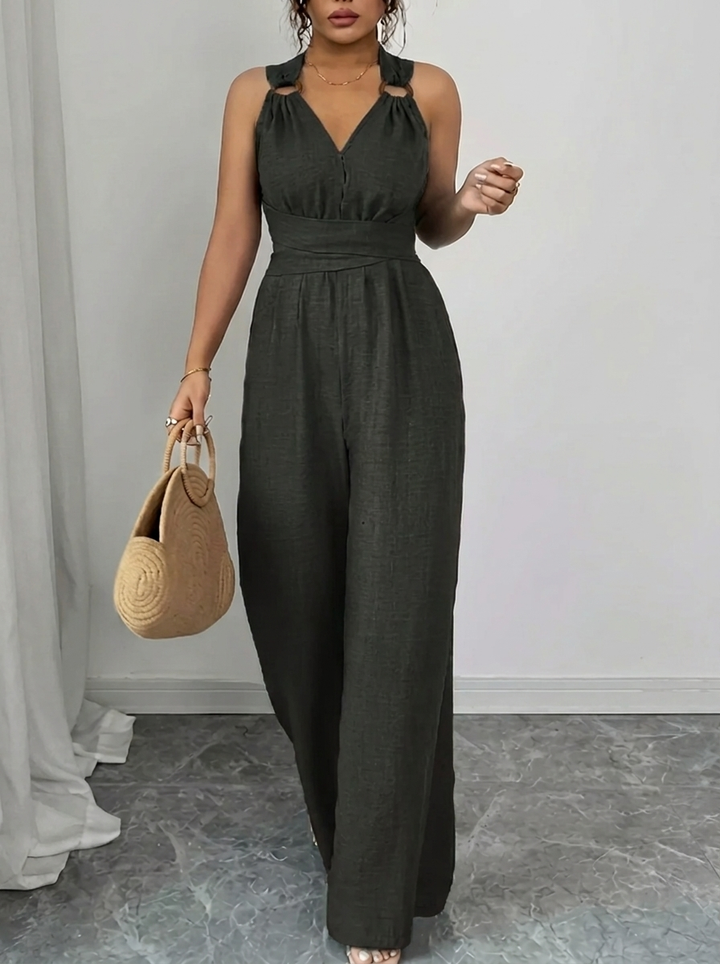 Woman wearing a dark green jumpsuit holding a beige handbag indoors.