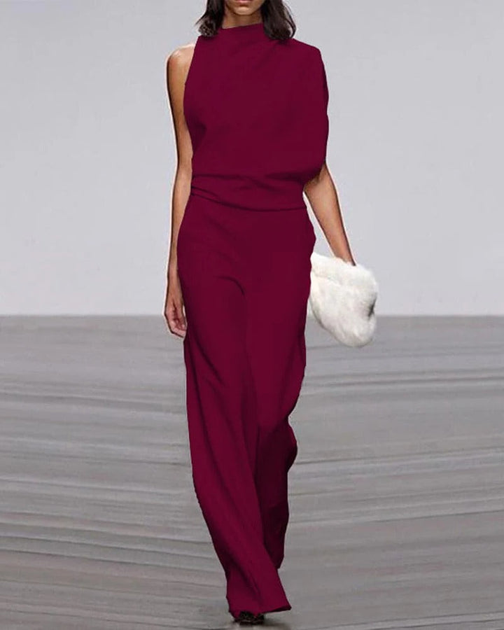 Woman wearing a burgundy jumpsuit with a white fur clutch on a gray floor.