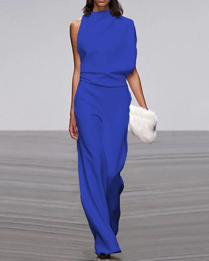 Woman wearing a blue jumpsuit holding a white fur clutch on a gray floor.