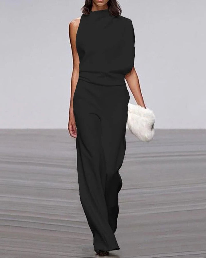 Woman wearing a black jumpsuit with a white fur clutch on a gray background