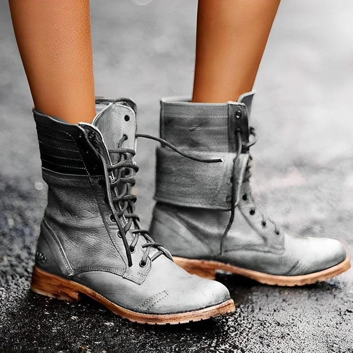 Gray combat boots with brown soles worn by a person on a gray background