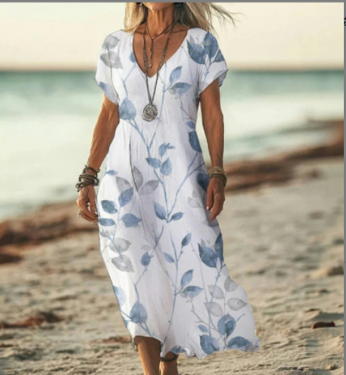 Woman wearing a white dress with blue floral patterns on a beach.