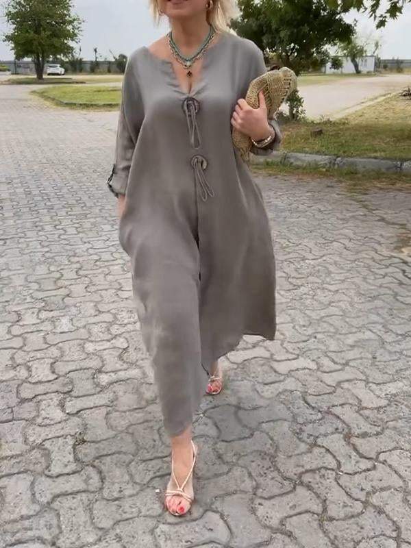 Woman in a long gray dress walking on a paved road with trees and grass in the background.