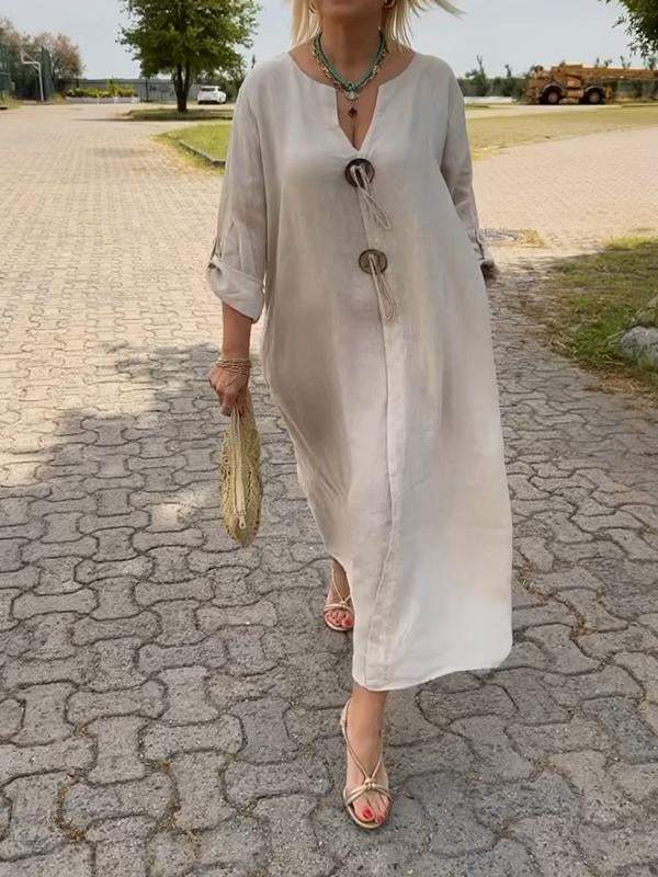 Woman in a long beige dress walking on a paved road.