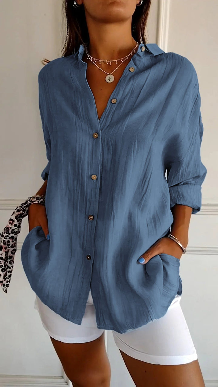 Woman wearing a blue button-up shirt and white shorts with a neutral background