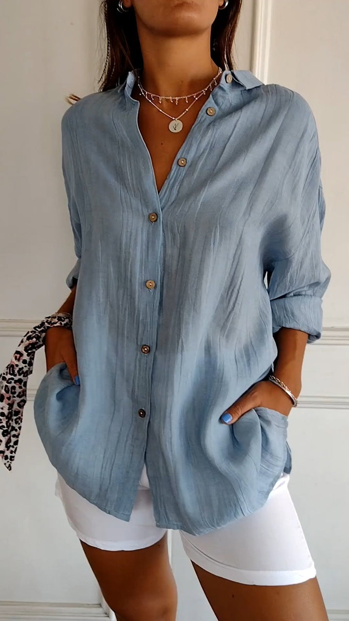 Woman wearing a light blue button-up shirt with rolled-up sleeves and white shorts.