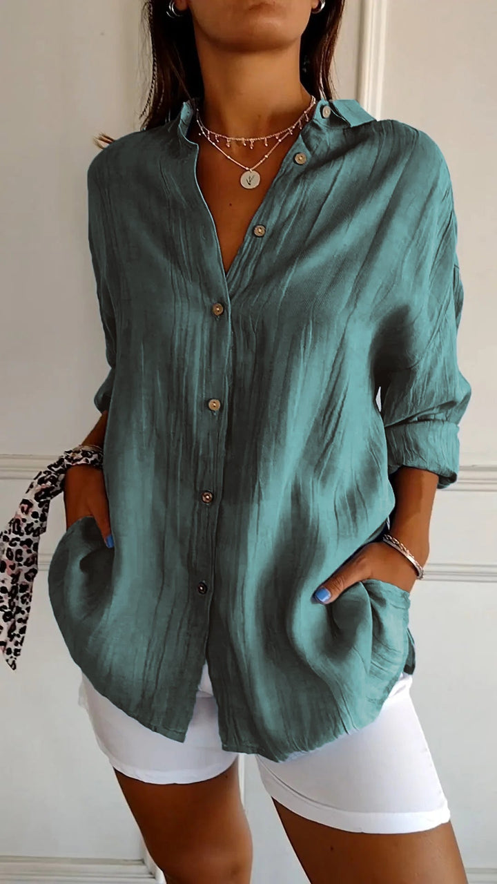 Person wearing a teal button-up shirt with white shorts indoors.