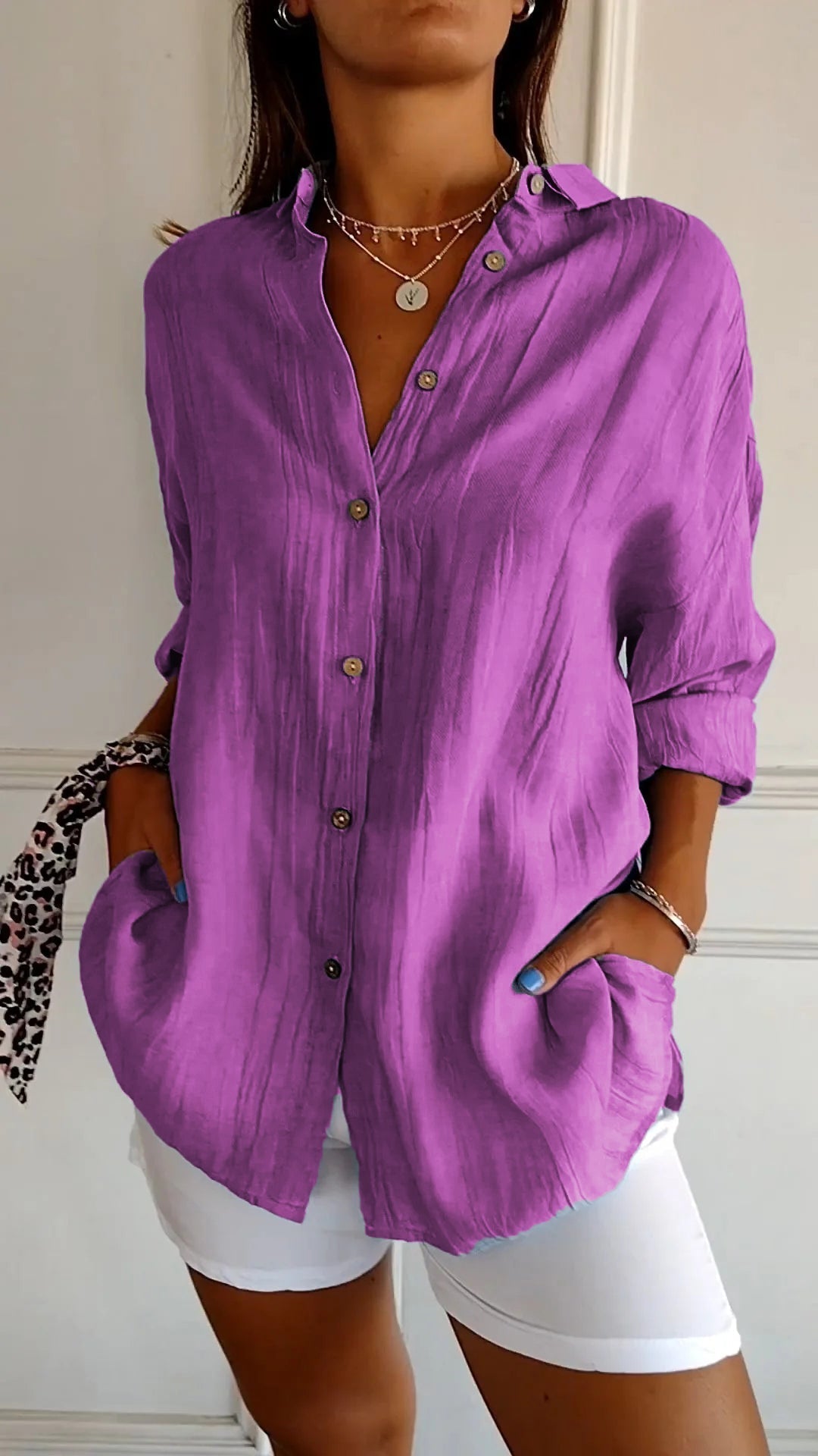 Person wearing a purple button-up shirt and white shorts indoors.