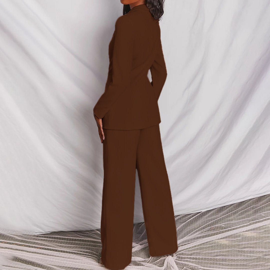 Person wearing a brown suit standing against a white curtain.