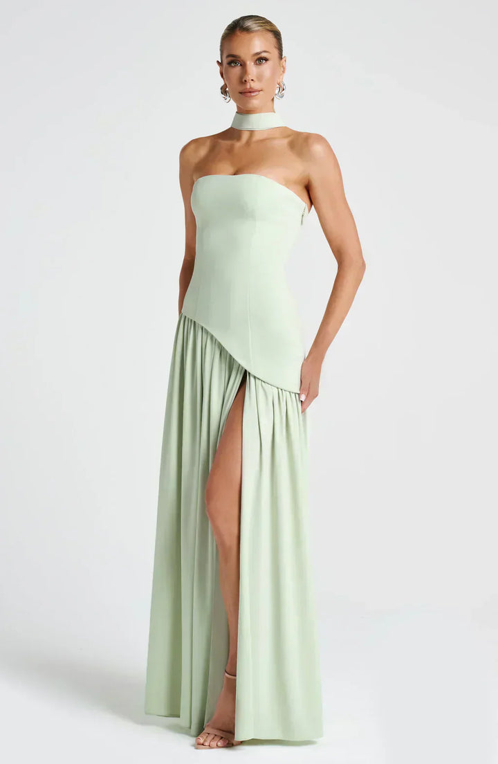 Woman wearing a strapless, light green evening gown with a slit on a white background