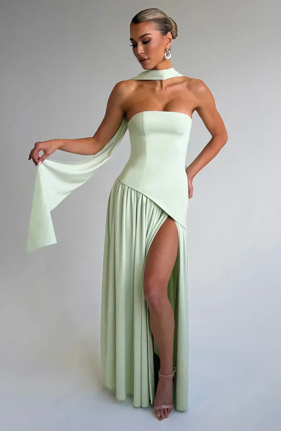 Woman wearing a light green evening gown with a slit on a plain background