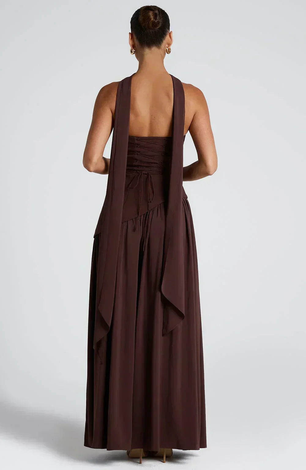 Woman wearing a long brown dress with a halter neck design on a white background