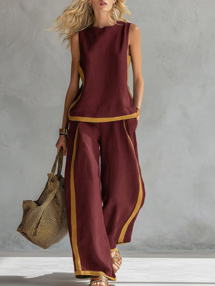 Woman wearing a burgundy outfit with gold trim, holding a textured bag against a gray background.