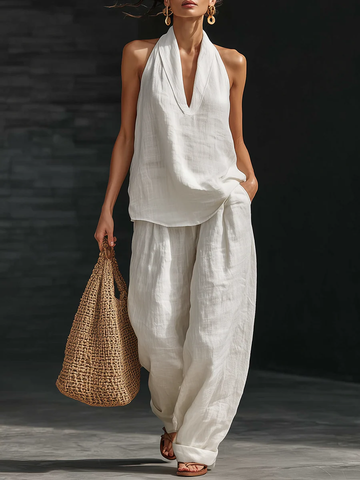 Woman in a white outfit holding a woven bag against a dark background