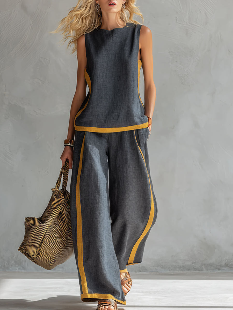 Woman wearing a gray sleeveless top and wide-leg pants with yellow accents, holding a textured bag against a neutral background.