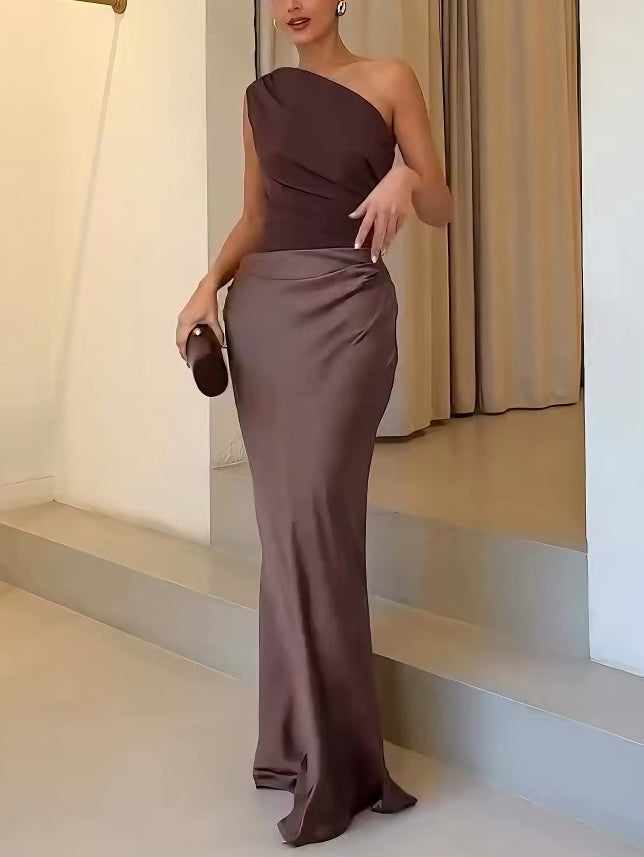 Woman in a brown one-shoulder dress standing on a staircase.