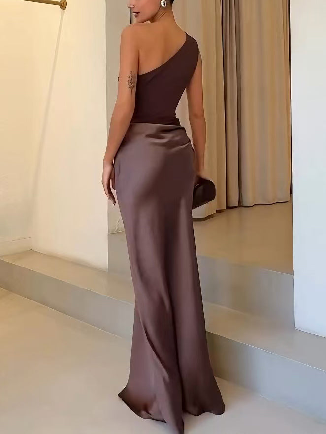 Woman in a brown one-shoulder dress standing on a staircase.