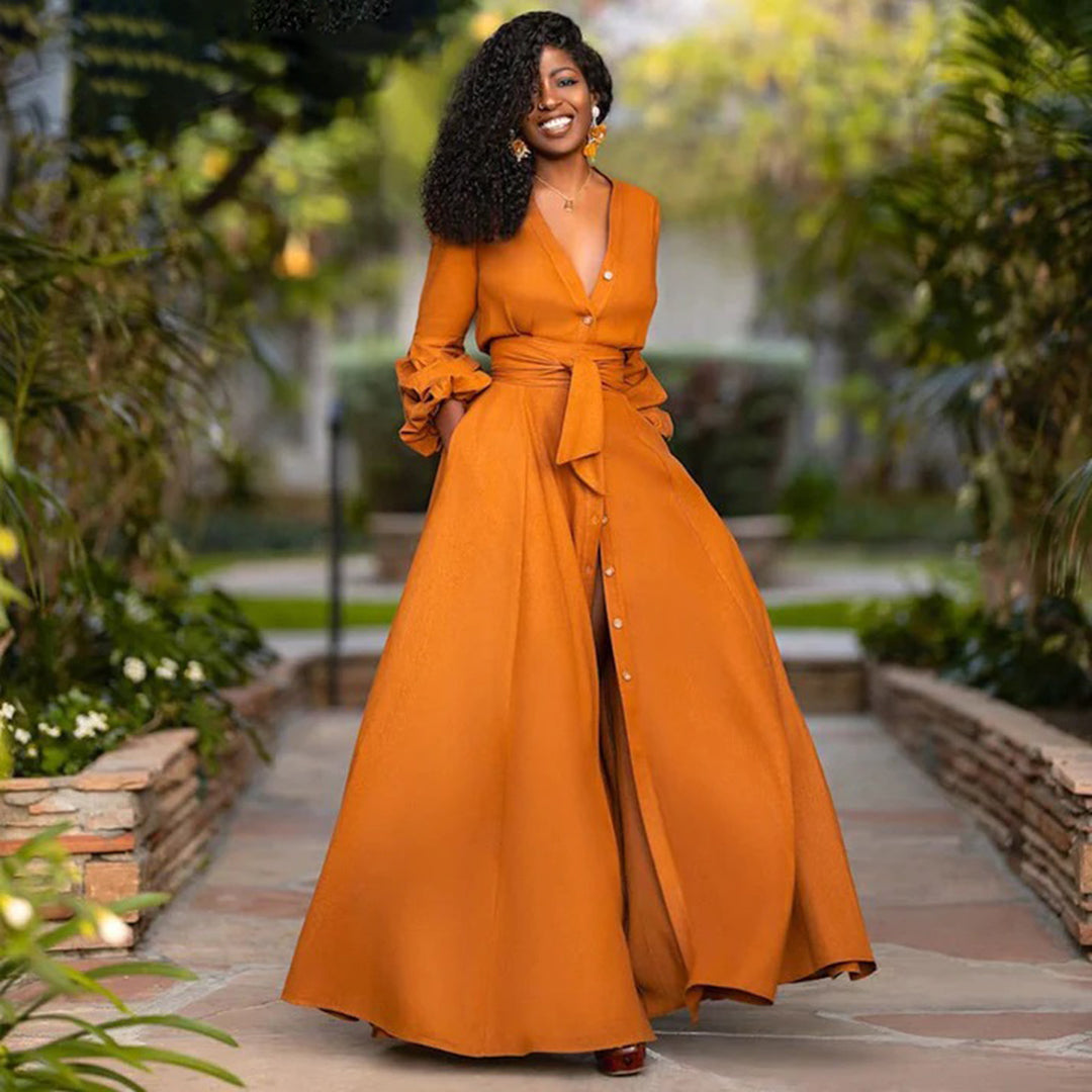 Woman in an orange dress standing outdoors with greenery in the background