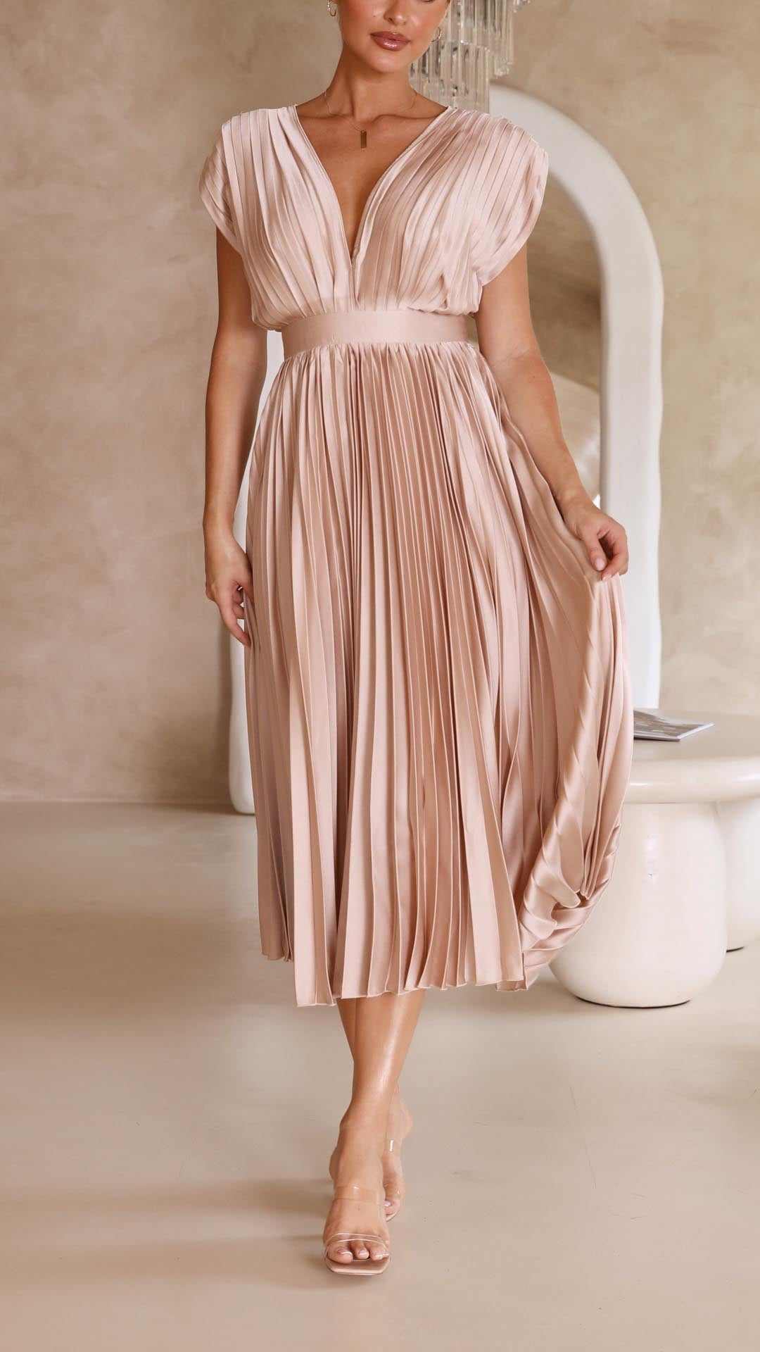Woman wearing a blush pink pleated dress against a neutral background
