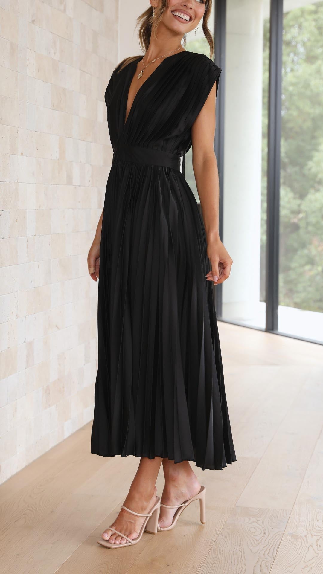 Woman wearing a black dress standing indoors with a light background
